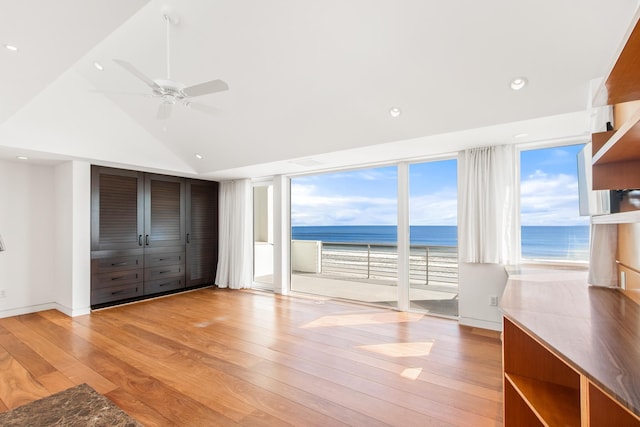 unfurnished bedroom with ceiling fan, a water view, a view of the beach, and light wood-type flooring