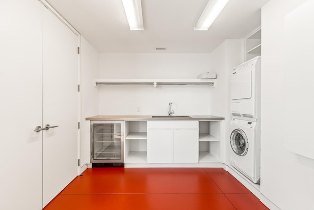 laundry area featuring cabinets, beverage cooler, stacked washer and clothes dryer, and sink