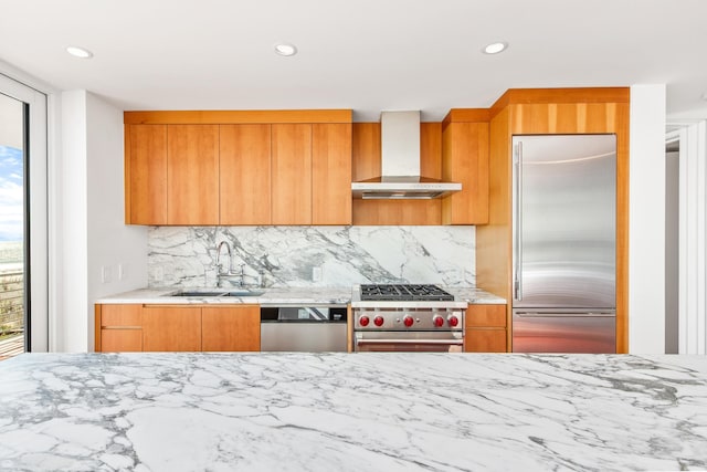 kitchen with high quality appliances, sink, wall chimney exhaust hood, and plenty of natural light