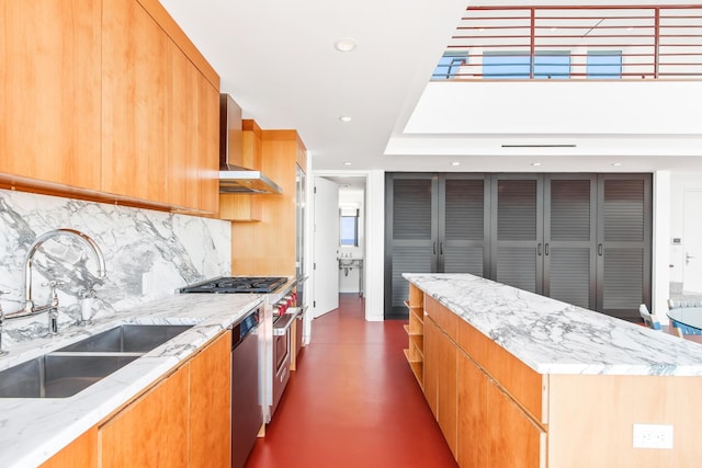 kitchen with sink, wall chimney exhaust hood, light stone counters, decorative backsplash, and a kitchen island