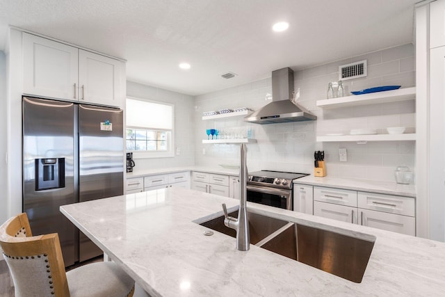 kitchen featuring white cabinetry, stainless steel appliances, a kitchen breakfast bar, light stone countertops, and wall chimney exhaust hood