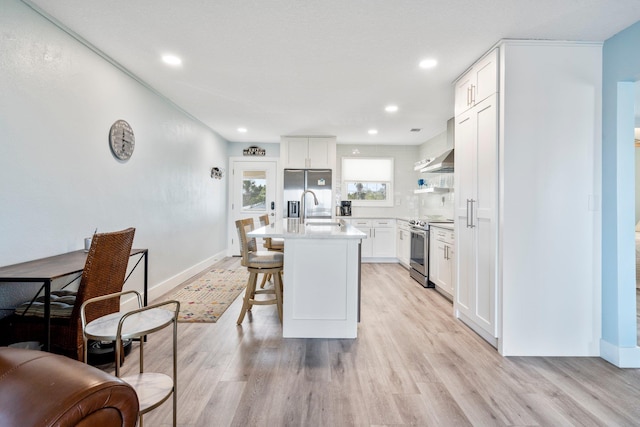 kitchen with appliances with stainless steel finishes, a breakfast bar area, white cabinets, light hardwood / wood-style floors, and a center island with sink