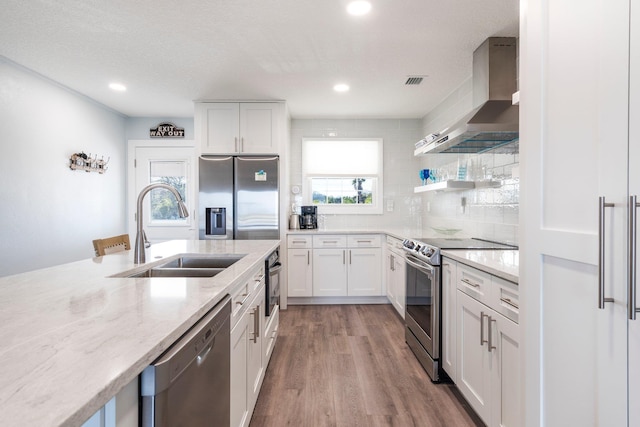 kitchen with stainless steel appliances, sink, white cabinets, and wall chimney exhaust hood