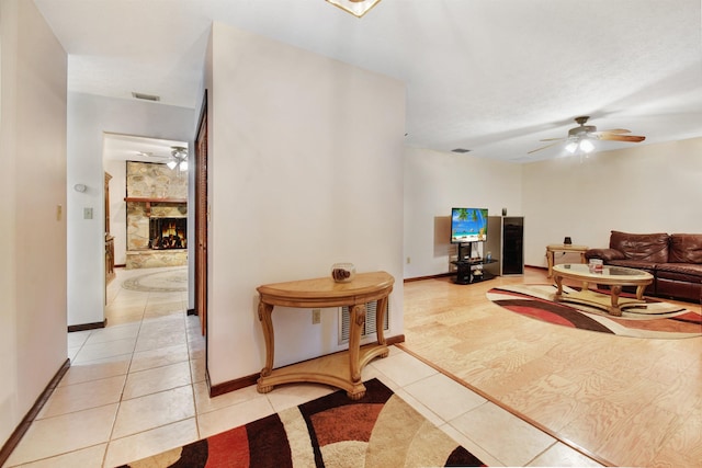 tiled living room featuring a stone fireplace and ceiling fan