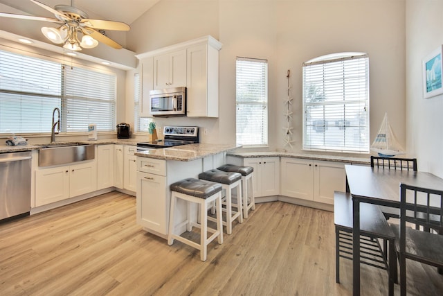 kitchen featuring sink, vaulted ceiling, light stone counters, white cabinetry, and stainless steel appliances