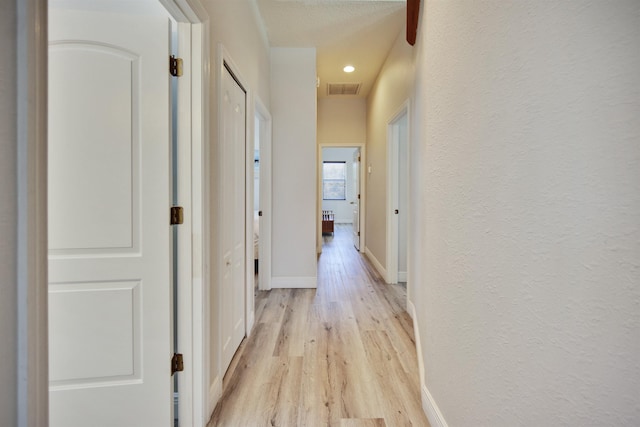 corridor with a textured ceiling and light wood-type flooring