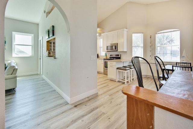 kitchen with appliances with stainless steel finishes, high vaulted ceiling, light hardwood / wood-style floors, and white cabinetry