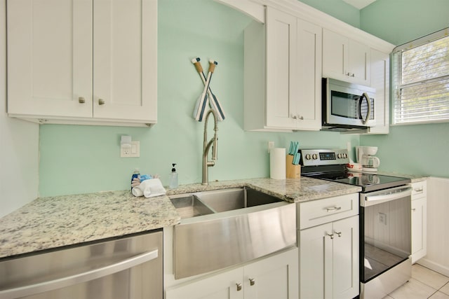 kitchen with light stone countertops, appliances with stainless steel finishes, sink, white cabinetry, and light tile patterned flooring