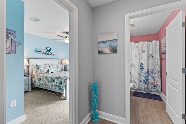 bedroom featuring ceiling fan, ensuite bath, wood-type flooring, and a textured ceiling