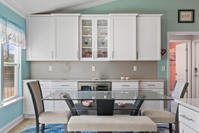 kitchen with white cabinetry, crown molding, vaulted ceiling, and tasteful backsplash