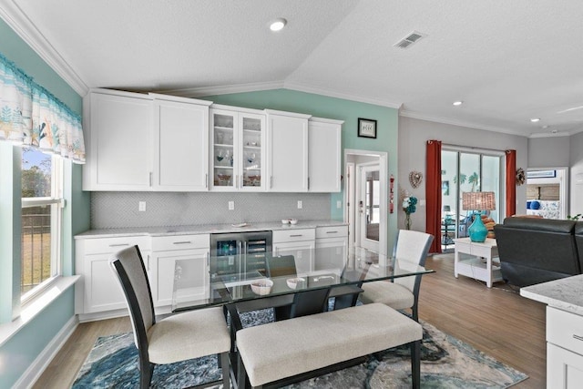 dining room with wine cooler, vaulted ceiling, ornamental molding, and light hardwood / wood-style flooring