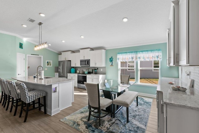 dining area featuring lofted ceiling, sink, ornamental molding, light hardwood / wood-style floors, and a textured ceiling