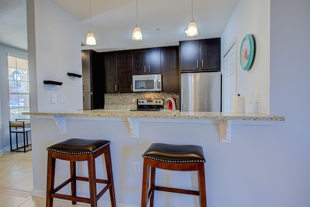 kitchen featuring kitchen peninsula, stainless steel appliances, tasteful backsplash, dark brown cabinetry, and a breakfast bar