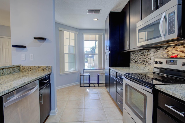 kitchen featuring light stone countertops, a textured ceiling, appliances with stainless steel finishes, backsplash, and light tile patterned floors