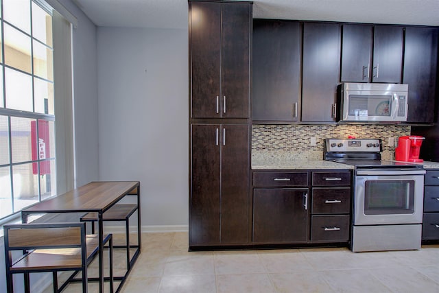 kitchen with stainless steel appliances, tasteful backsplash, light tile patterned flooring, light stone counters, and dark brown cabinetry