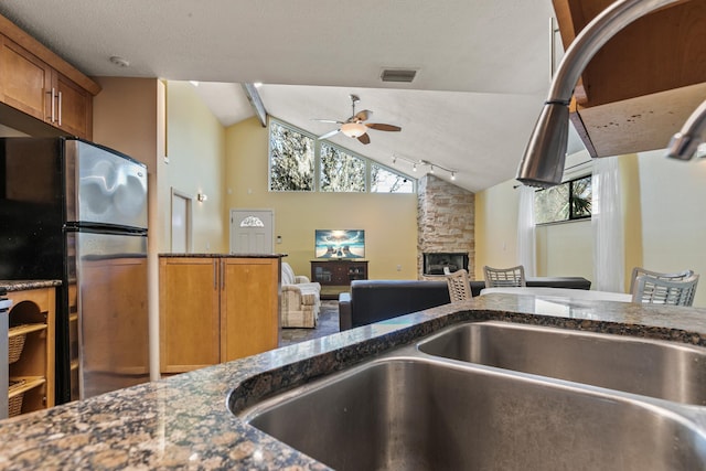 29 Hybiscus Ave, Saint Augustine, FL 32084 - kitchen featuring freestanding refrigerator, ceiling fan, brown cabinets, a stone fireplace, and dark stone countertops