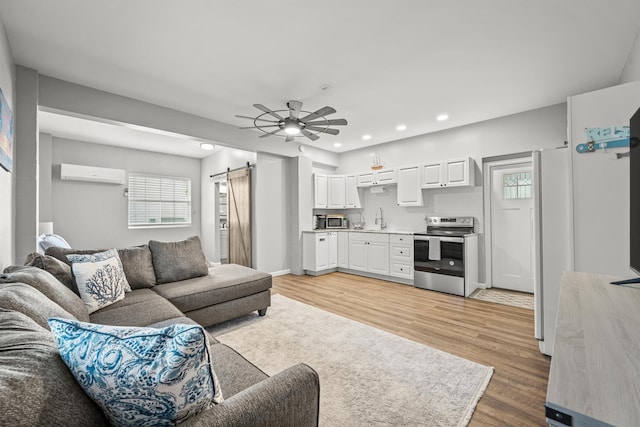 living room with light wood-type flooring, a wall unit AC, ceiling fan, sink, and a barn door