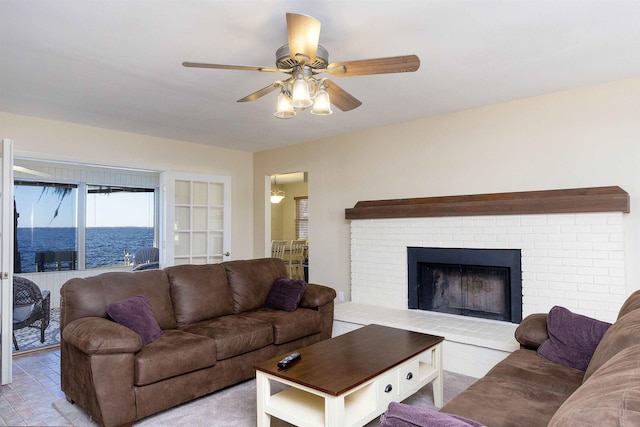 living room featuring ceiling fan, a water view, and a brick fireplace