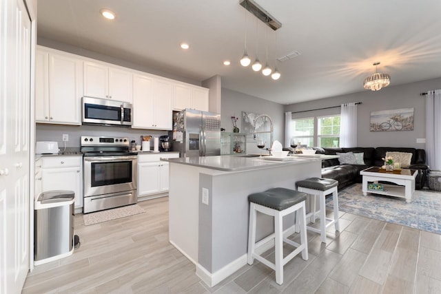 kitchen featuring pendant lighting, stainless steel appliances, white cabinetry, and a center island with sink