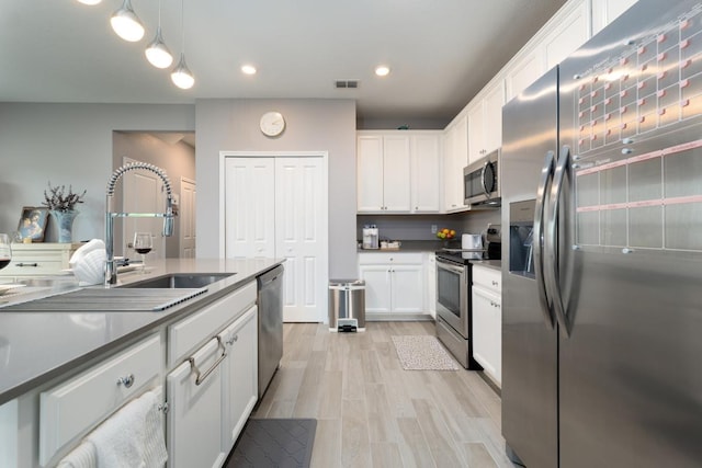 kitchen featuring light wood-type flooring, stainless steel appliances, sink, white cabinetry, and hanging light fixtures