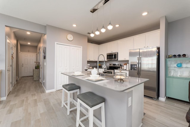 kitchen with white cabinetry, a kitchen island with sink, hanging light fixtures, and appliances with stainless steel finishes