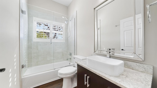 full bathroom featuring hardwood / wood-style flooring, vanity, shower / bath combination with glass door, and toilet