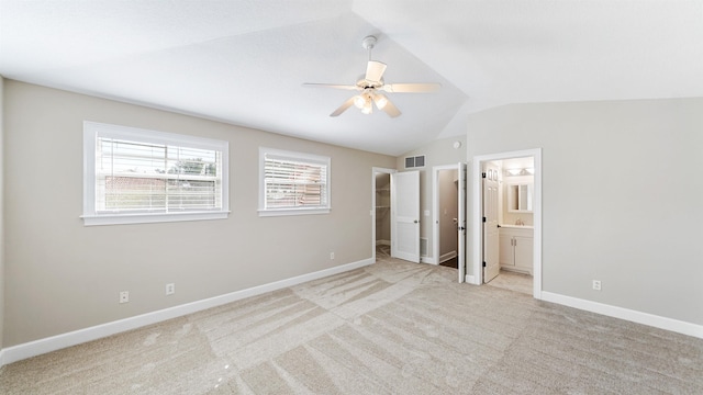 unfurnished bedroom featuring lofted ceiling, ensuite bath, ceiling fan, light carpet, and a walk in closet