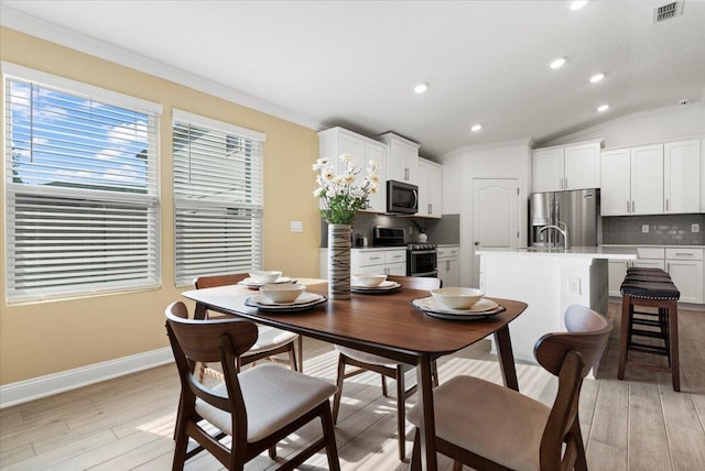 dining space with light hardwood / wood-style flooring, ornamental molding, and vaulted ceiling