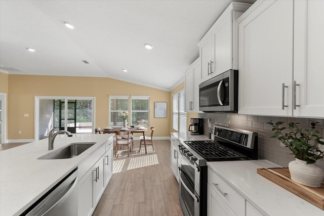 kitchen featuring sink, white cabinetry, vaulted ceiling, stainless steel appliances, and decorative backsplash