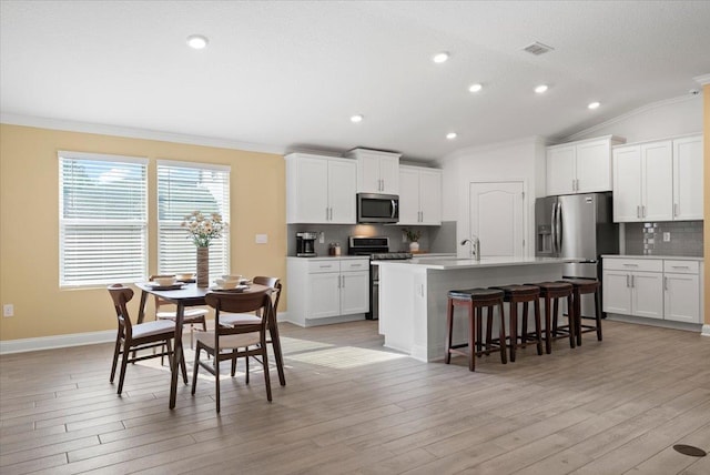 kitchen with a kitchen island with sink, white cabinetry, a breakfast bar area, and stainless steel appliances