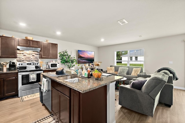 kitchen featuring stainless steel appliances, sink, stone countertops, a center island with sink, and light hardwood / wood-style floors