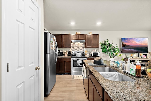 kitchen with appliances with stainless steel finishes, light wood-type flooring, light stone counters, dark brown cabinetry, and sink