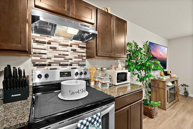 kitchen with stainless steel electric range oven, light hardwood / wood-style flooring, dark stone counters, extractor fan, and dark brown cabinets