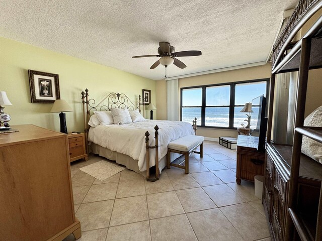 tiled bedroom with ceiling fan, a water view, and a textured ceiling