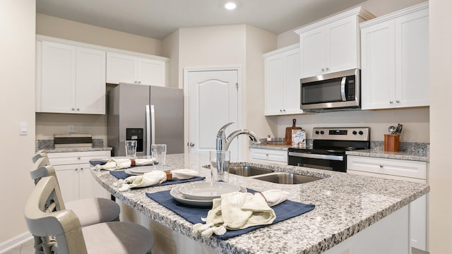 kitchen with sink, white cabinetry, light stone counters, an island with sink, and stainless steel appliances