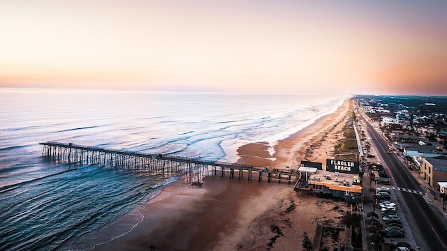 aerial view at dusk with a water view and a view of the beach