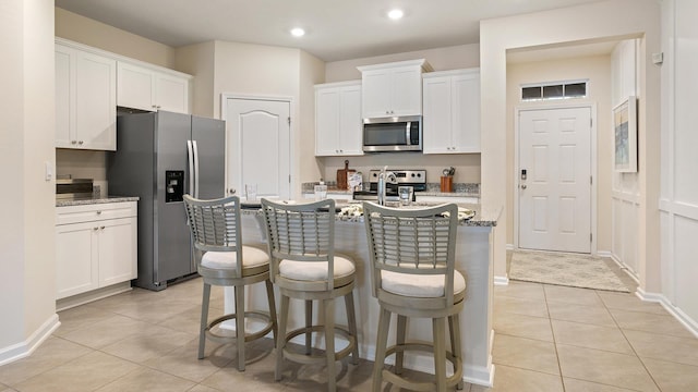 kitchen with white cabinetry, stainless steel appliances, light stone countertops, and light tile patterned floors