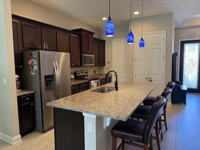 kitchen featuring dark brown cabinetry, appliances with stainless steel finishes, light stone countertops, a sink, and light tile patterned flooring