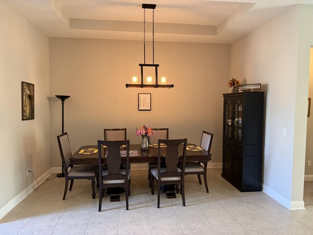 dining space featuring light tile patterned floors, a tray ceiling, an inviting chandelier, and baseboards