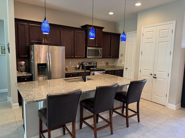 kitchen featuring a kitchen breakfast bar, stainless steel appliances, dark brown cabinets, a sink, and light tile patterned flooring