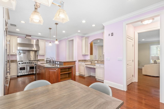 kitchen with a kitchen island with sink, wall chimney range hood, pendant lighting, double oven range, and stone counters