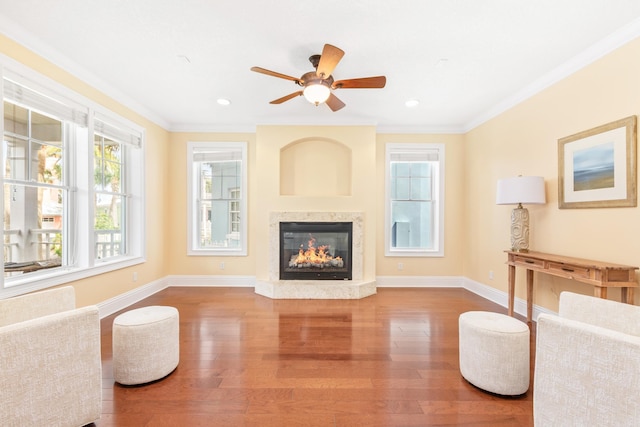 living room featuring ceiling fan, crown molding, a high end fireplace, and hardwood / wood-style flooring