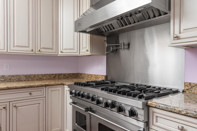 kitchen featuring light stone counters, cream cabinets, double oven range, and wall chimney range hood