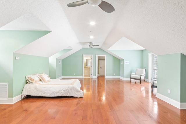 bedroom featuring a textured ceiling, vaulted ceiling, ceiling fan, hardwood / wood-style flooring, and connected bathroom