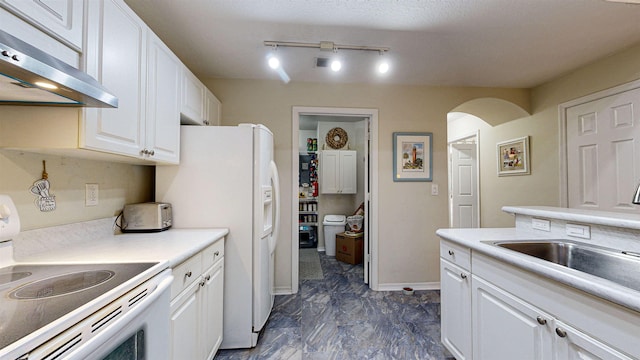 kitchen with white appliances, ventilation hood, sink, rail lighting, and white cabinetry