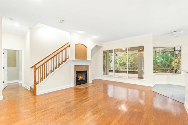 unfurnished living room with light hardwood / wood-style floors, ceiling fan, crown molding, and a tiled fireplace