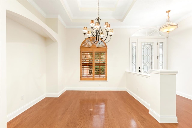 unfurnished dining area featuring hardwood / wood-style floors, a notable chandelier, a raised ceiling, and ornamental molding