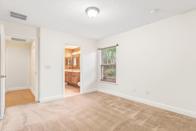 unfurnished bedroom with a textured ceiling, ensuite bathroom, and light colored carpet