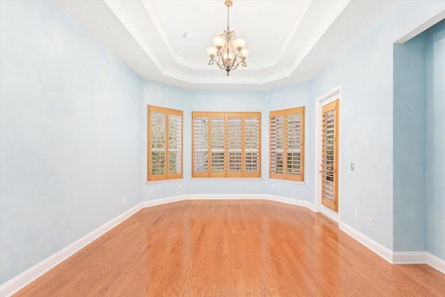 empty room featuring light wood-type flooring, a tray ceiling, and a notable chandelier