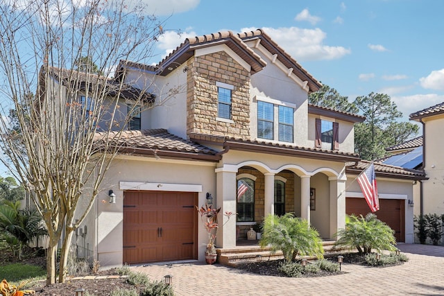 mediterranean / spanish house with a porch, stucco siding, a garage, a tile roof, and decorative driveway